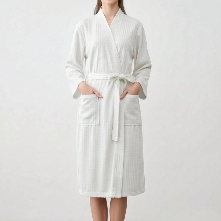 Model wearing the white version of the waffle-weave robe, hands in the patch pockets, belt tied in a bow at the waist. 7