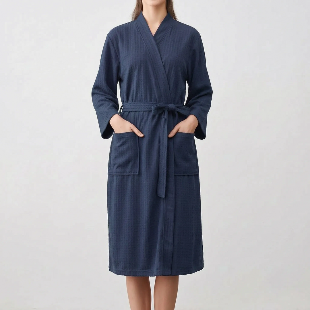 Model wearing the navy version of the waffle-weave robe, hands in the patch pockets, belt tied in a bow at the waist. 8
