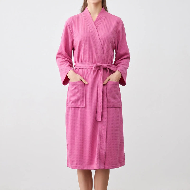 Model wearing the bright pink version of the waffle-weave robe, hands in the patch pockets, belt tied in a bow at the waist. 9