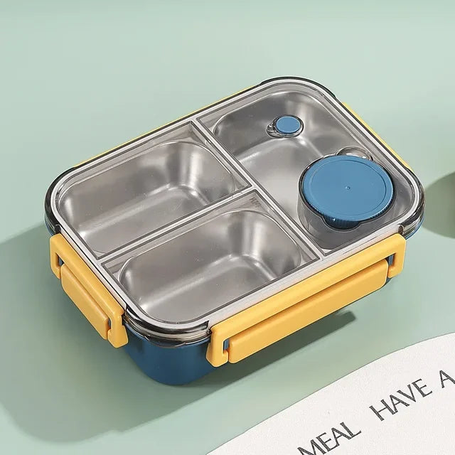 Top view of the navy and yellow container with empty steel compartments, a blue sauce cup and a clear lid on a green background.