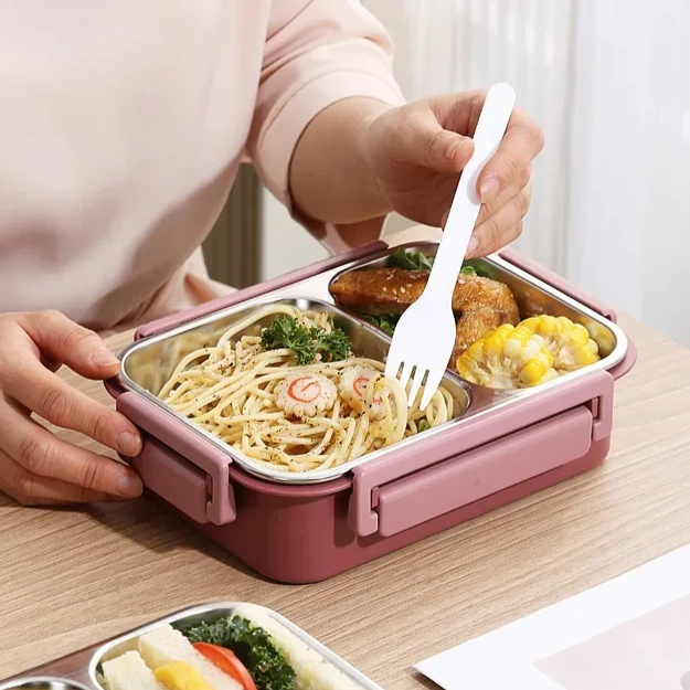 another view of person in a pink top eating noodles with a white fork from a pink container, with corn and chicken in the other compartment.
