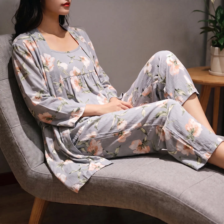 Woman reclining on a gray armchair in a gray floral robe, camisole and cropped pants with pink blooms, cropped at the face. 1