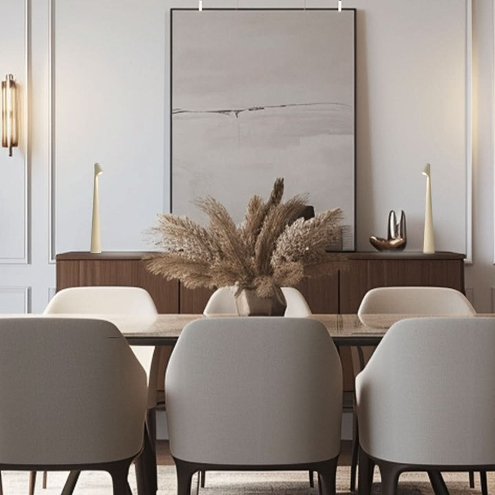 A cream lamp at each end of a wooden sideboard behind a dining table with pampas grass and large abstract art. 10