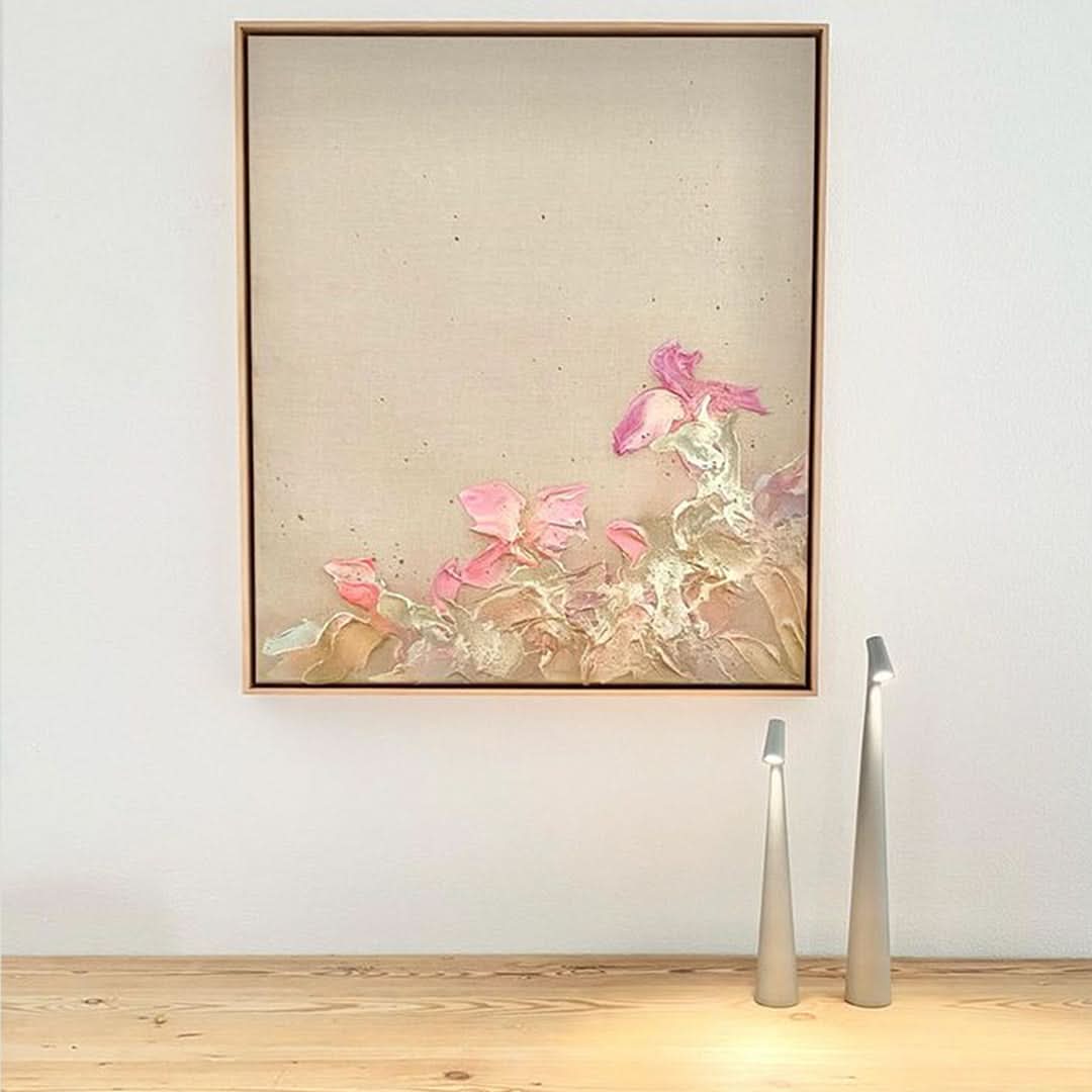 Two silver-gray lamps of different heights on a wooden surface below a framed pink floral textured painting. 11