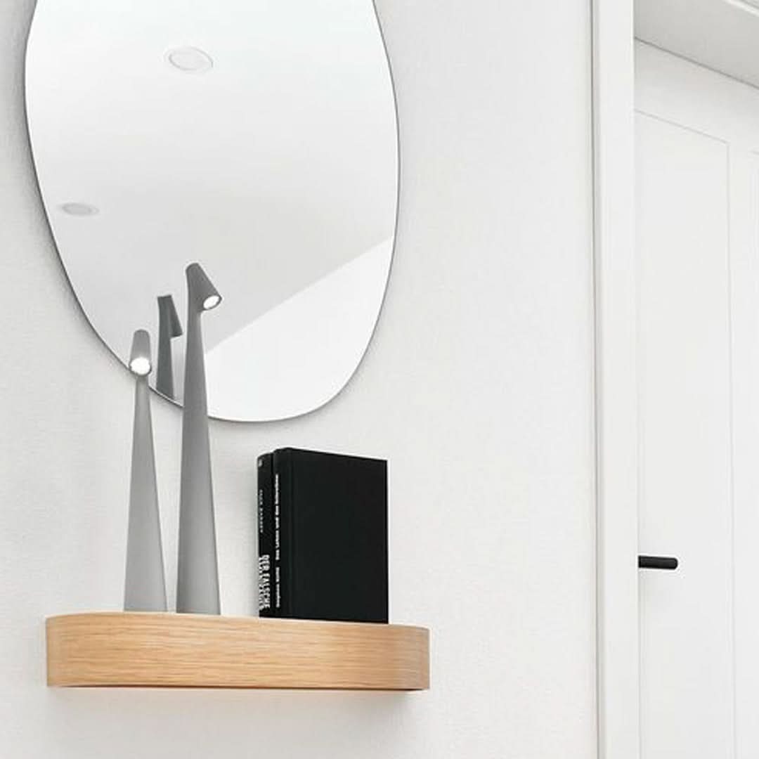 Two gray lamps lit on a small oak wall shelf beside a black book, with an oval mirror above. 12