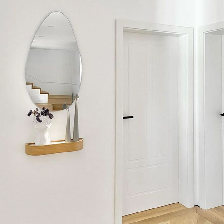 Two gray lamps and a white face-shaped vase with dark flowers on an oak wall shelf under an oval mirror in a hallway. 14