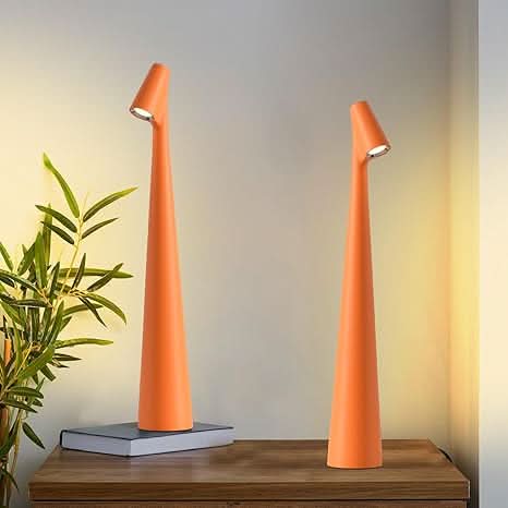 Two orange lamps lit on a wooden console table, one resting on a book, beside a bamboo plant. 15