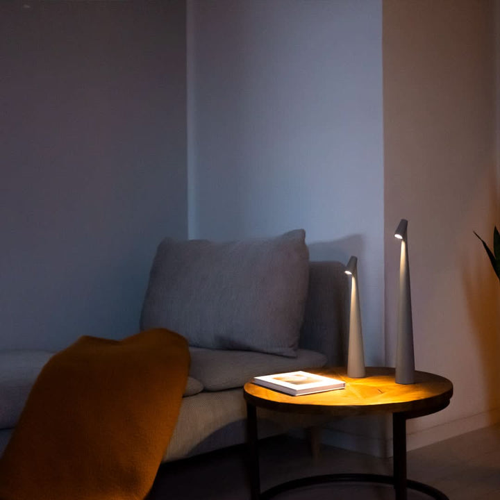 Two pale gray lamps lit on a round wooden side table beside a sofa, an open book and an orange throw. 5