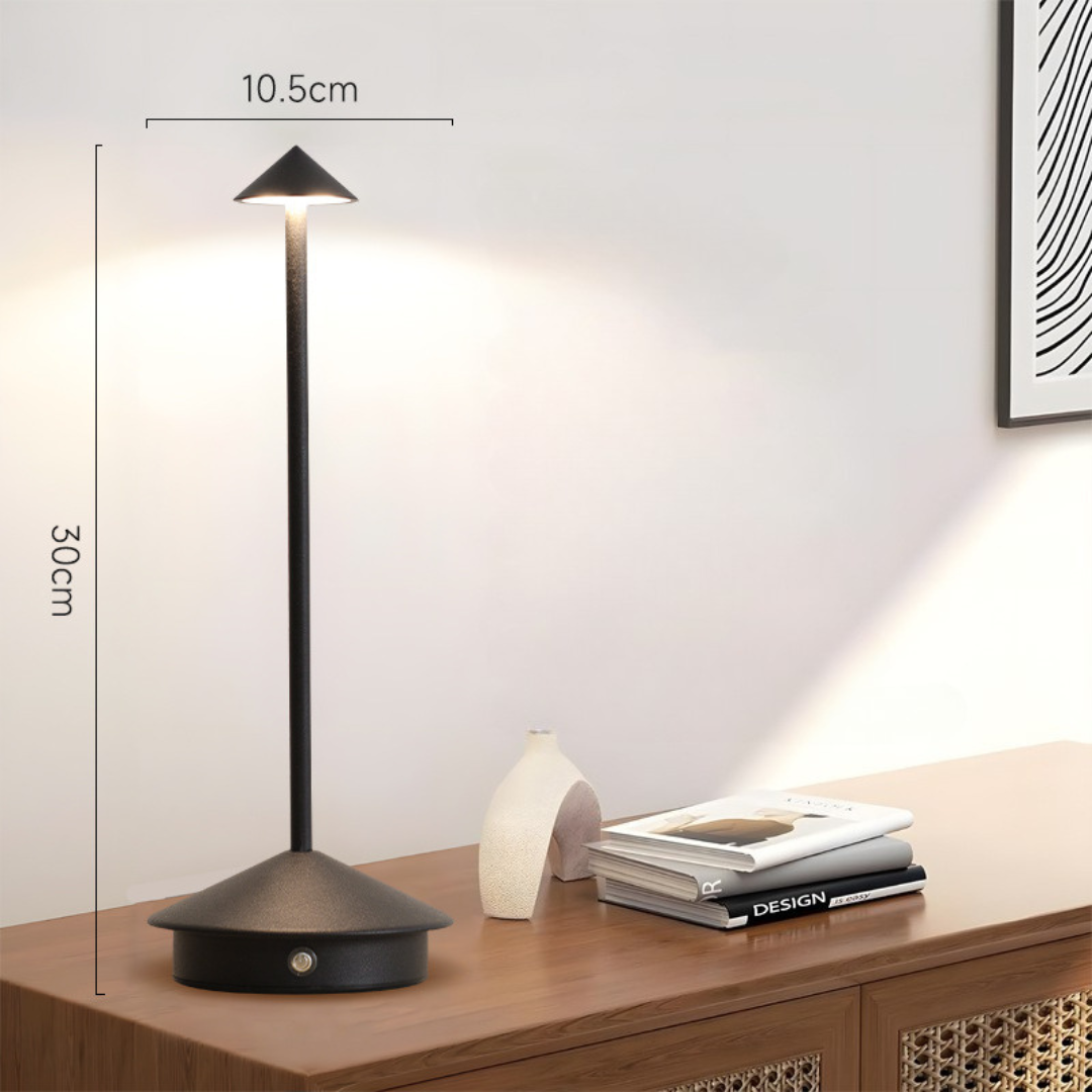 Black lamp lit on a wooden sideboard with height and width dimension lines beside a vase and books.