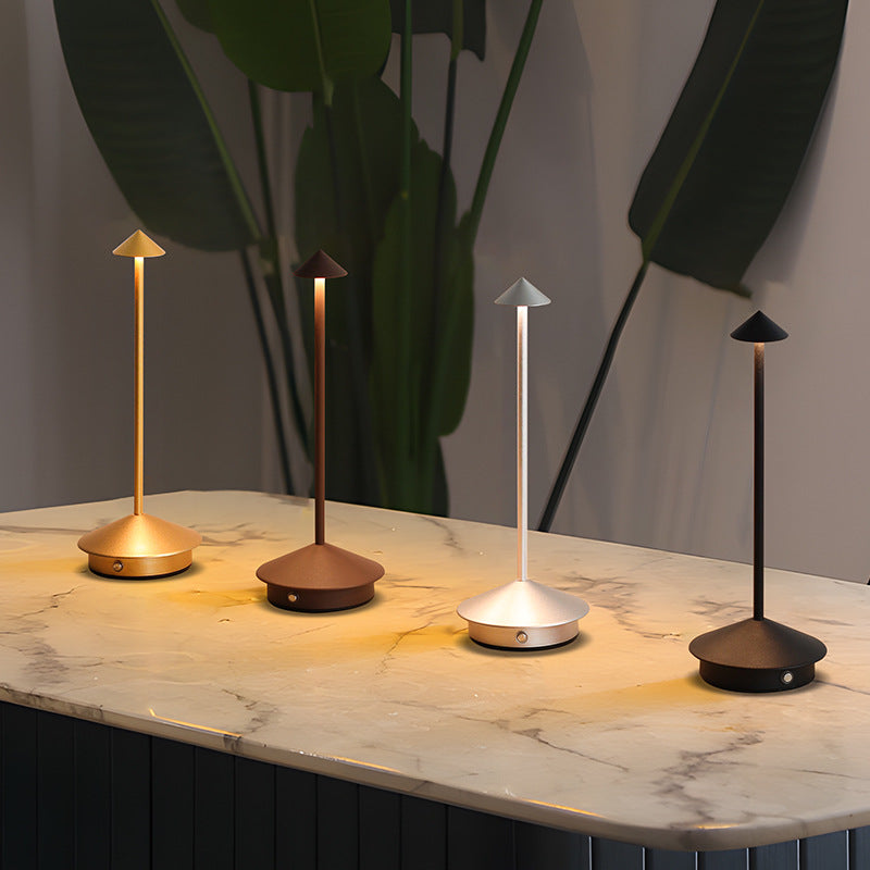 Four lit lamps in gold, brown, silver and black standing in a row on a marble tabletop.