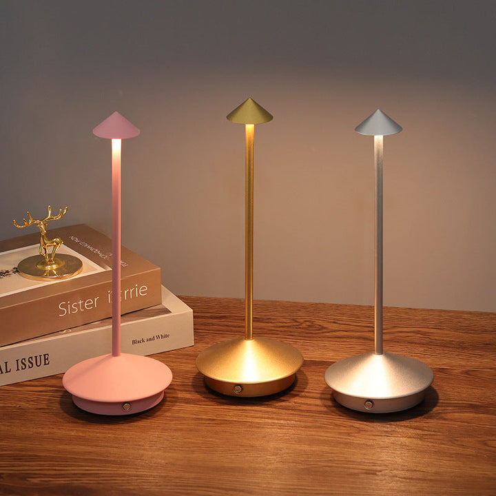 Pink, gold and silver lamps glowing side by side on a wooden surface next to a small stack of books.