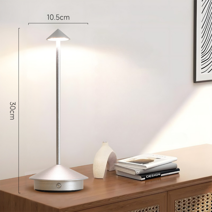 Silver lamp lit on a wooden sideboard with height and width dimension lines beside a vase and books.