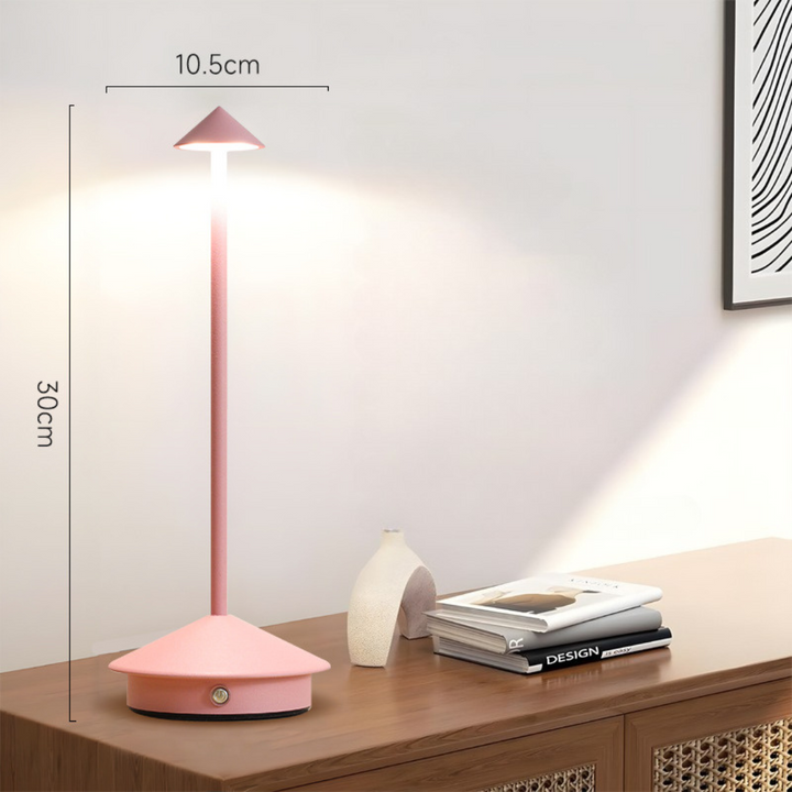 Pink lamp lit on a wooden sideboard with height and width dimension lines beside a vase and books.