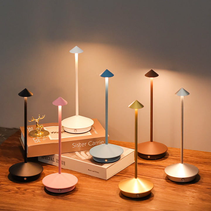 Seven slim cone-topped multicolor lamps glowing on a wooden table beside stacked books.