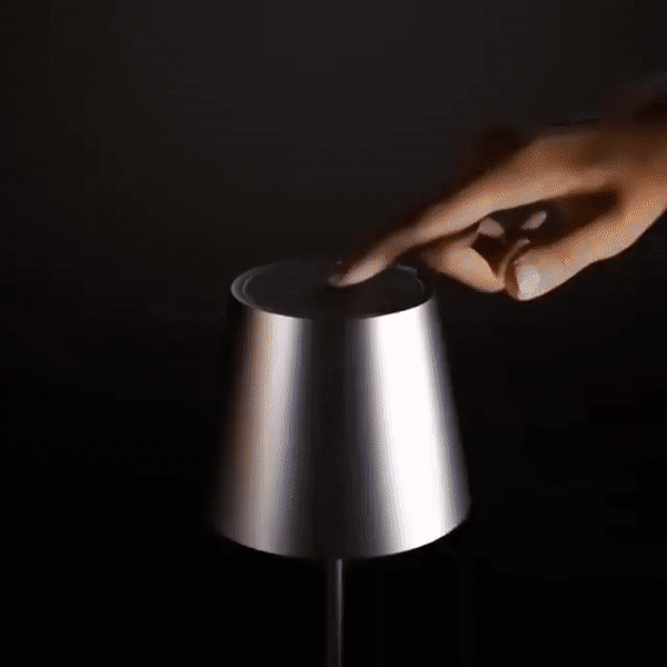 Detail of a hand touching the top of a silver lamp shade.