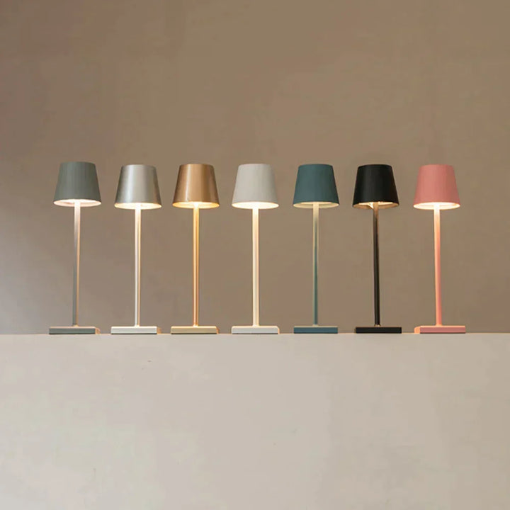Row of seven lit lamps in gray, silver, gold, white, teal, black and pink.
