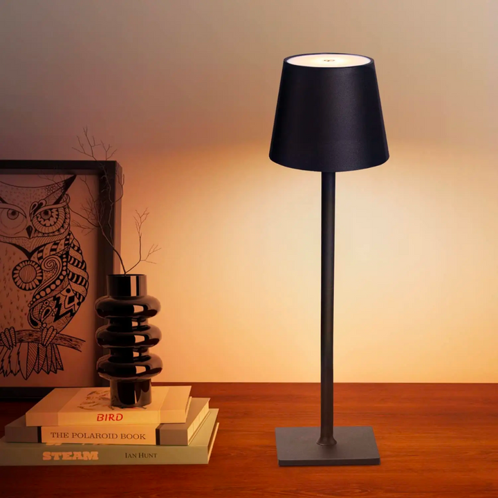 Black cordless table lamp with a tapered shade and square base on a wooden desk.