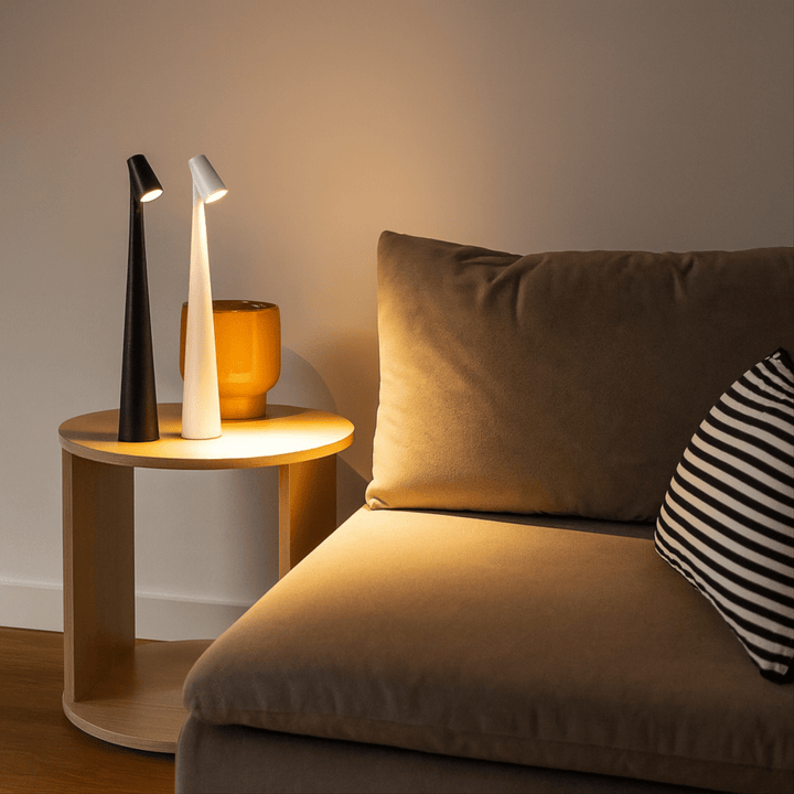 Red cordless table lamps glowing on a round wooden side table next to an amber vase.