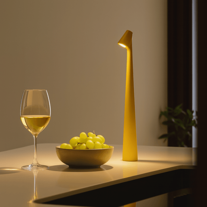 Red cordless table lamp lit on a countertop beside a glass of white wine and a bowl of green grapes.