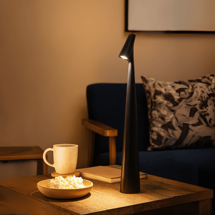 Red cordless table lamp lit on a rustic wooden side table beside a mug, a bowl of popcorn and a book.
