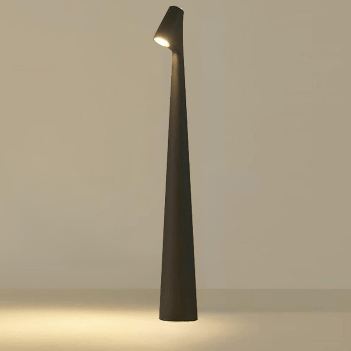 Red cordless table lamp with a slim tapered shape and angled head, lit against a neutral wall.