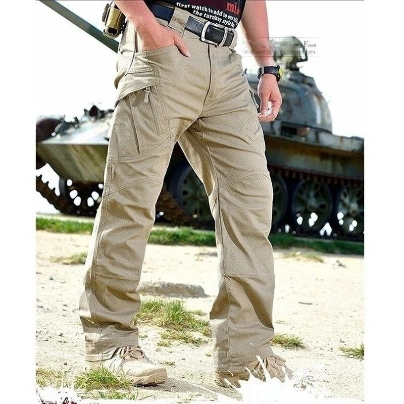 Men's khaki cargo pants front view on a model standing outdoors in front of a tank.