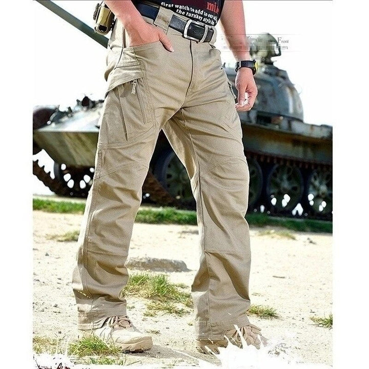 Men's khaki cargo pants front view on a model standing outdoors in front of a tank.
