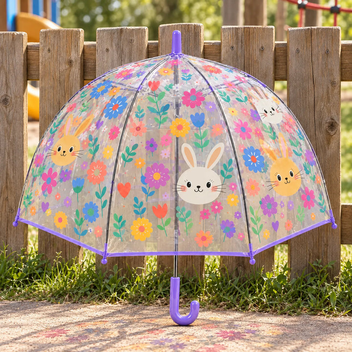 Clear dome umbrella with a purple trim and hook handle, printed with bunny faces and colorful flowers, standing against a wooden fence. 1