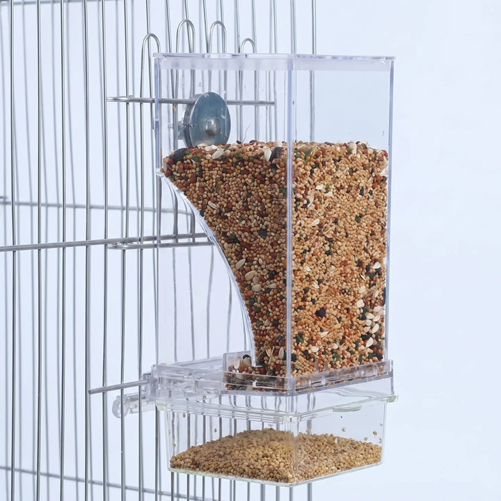 Clear acrylic seed feeder clipped to the wire bars of a cage, filled with mixed seeds and a tray below. 1