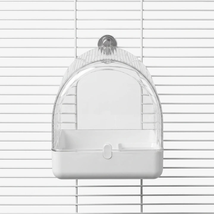 Front view of a clear arched bird bath with a white tray, mounted on white cage bars by a metal-colored fastener. 1