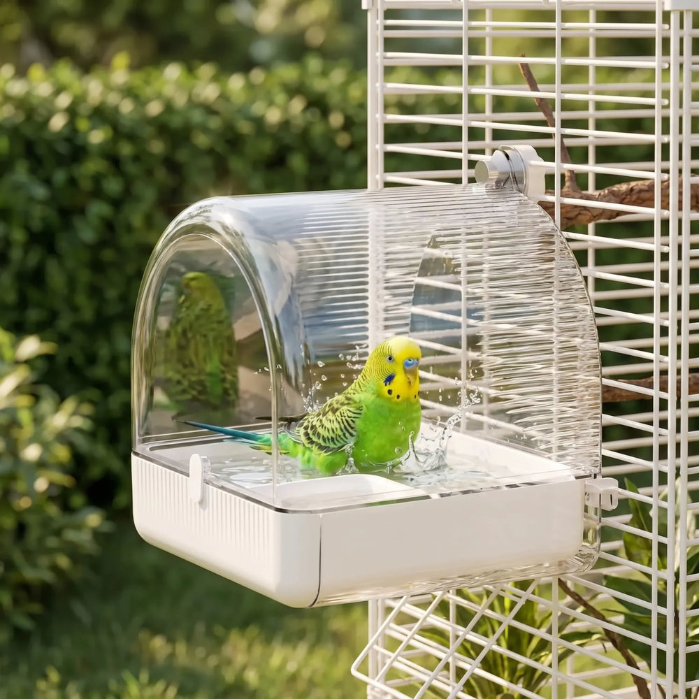A green and yellow budgie splashes in the bath attached to a white cage, with a leafy garden behind. 2