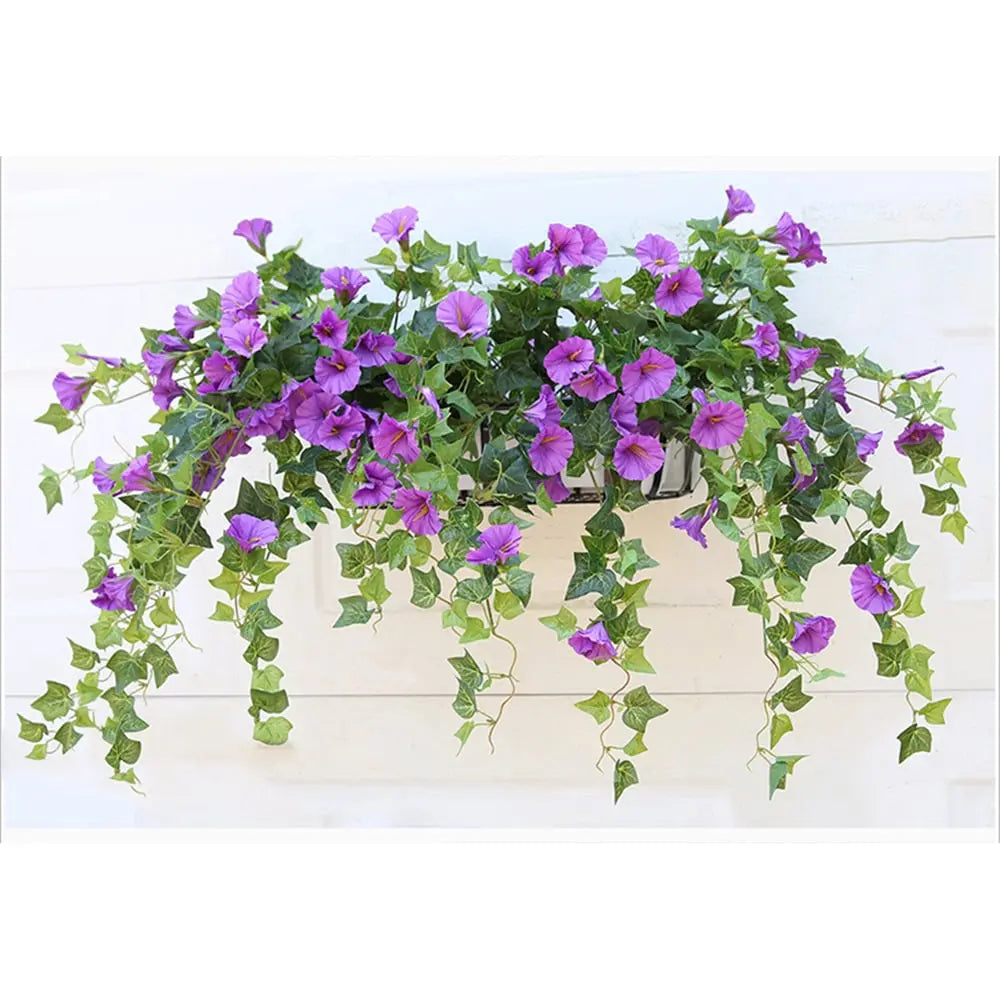 Purple faux morning glory flowers and trailing green vines spilling from a wall-mounted planter box against a white wall.