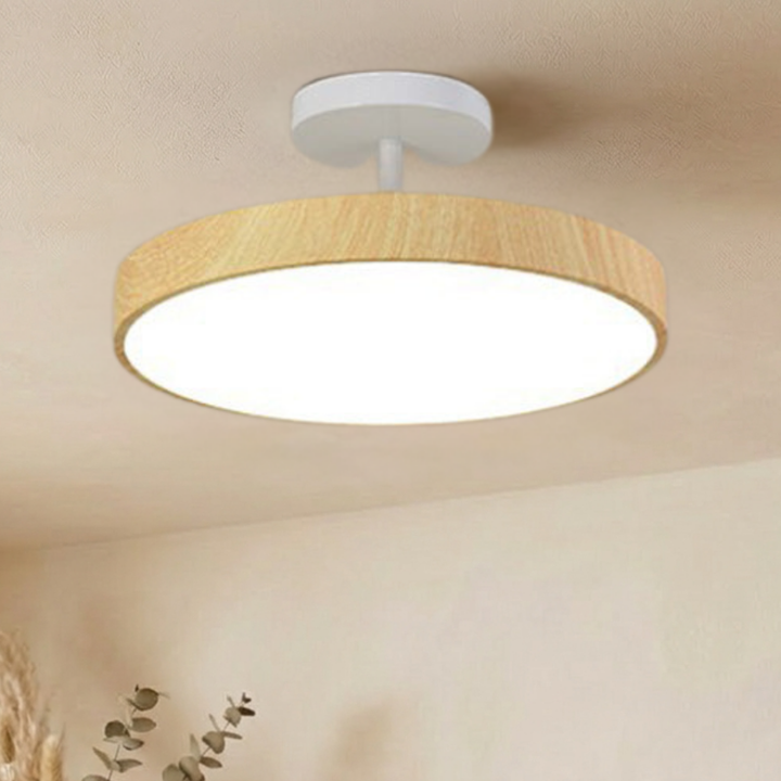 Light oak-look disc ceiling light with a white canopy and stem, shining bright white against a beige ceiling.
