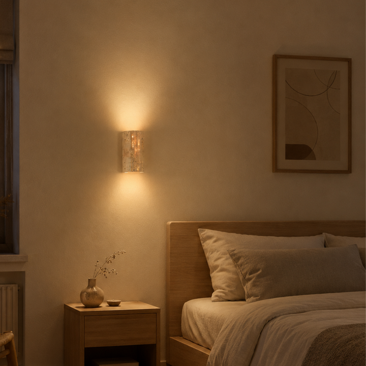 Natural Stone Wall Sconce Wall Light glowing on a bedroom wall above a wooden nightstand with a vase and framed art.