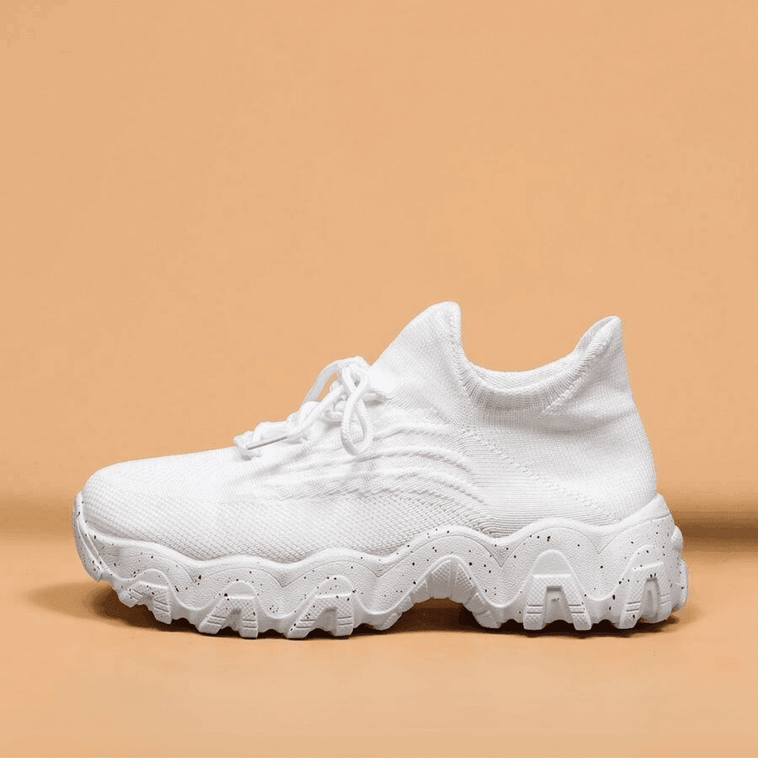 Another view of an all-white knit sneaker with white laces and a wavy chunky speckled sole.