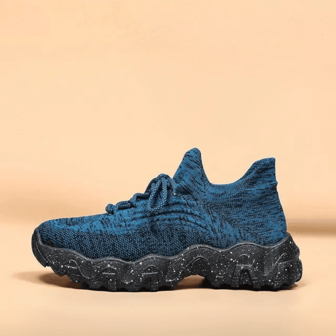Side view of a single blue marled knit sneaker with a black speckled chunky wavy sole on a peach background. 27