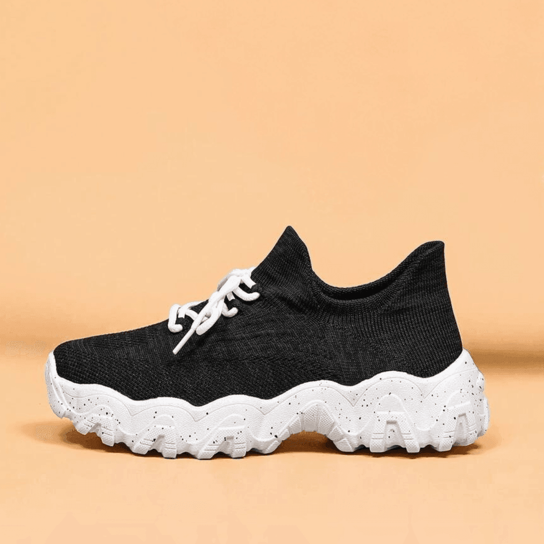 Side view of a single black knit sneaker with white laces and a thick white speckled wavy sole. 32