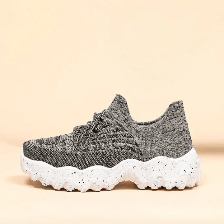 Side view of a single gray marled knit sneaker with a thick white speckled wavy sole on a cream background. 37