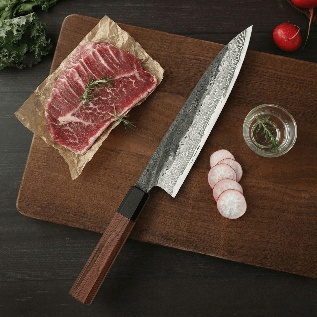 Kiritsuke knife another view on a walnut cutting board beside a raw steak with rosemary and sliced radishes.