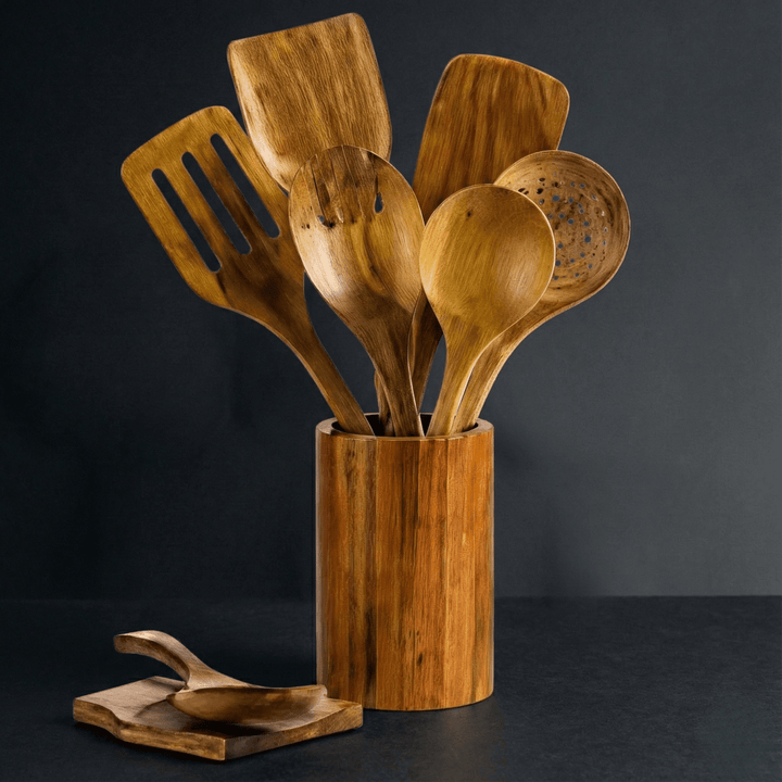 Wooden utensils standing in a cylindrical wooden holder with a spoon rest beside it.