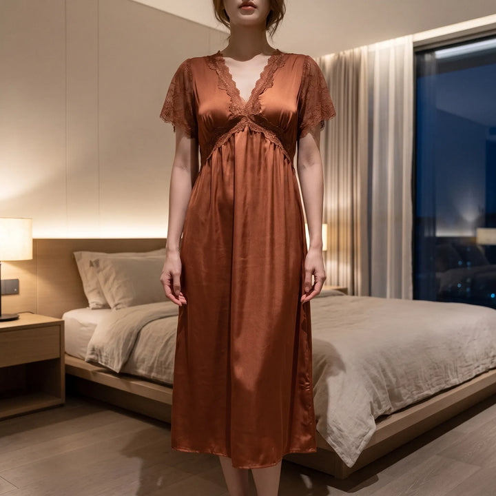 Model standing in a softly lit bedroom wearing the rust-brown satin nightgown with lace V-neck, waist trim and sheer lace sleeves. 1
