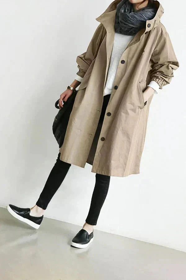 Tan waterproof hooded trench coat worn open at the bottom with black pants
