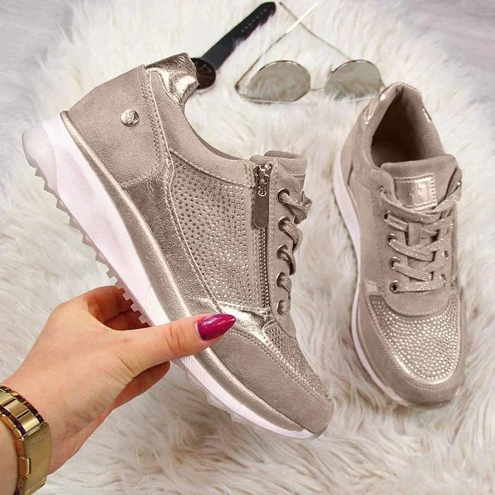 Another view of a taupe sneaker showing its side zipper and perforated panel, with the second shoe and accessories.