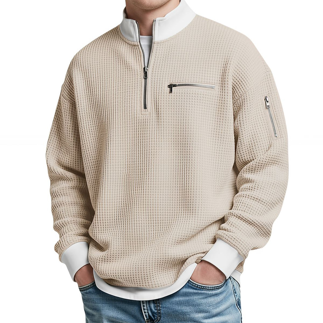 Front view of a beige waffle knit quarter-zip sweater with a white contrast collar, chest zip pocket and a zippered sleeve pocket.