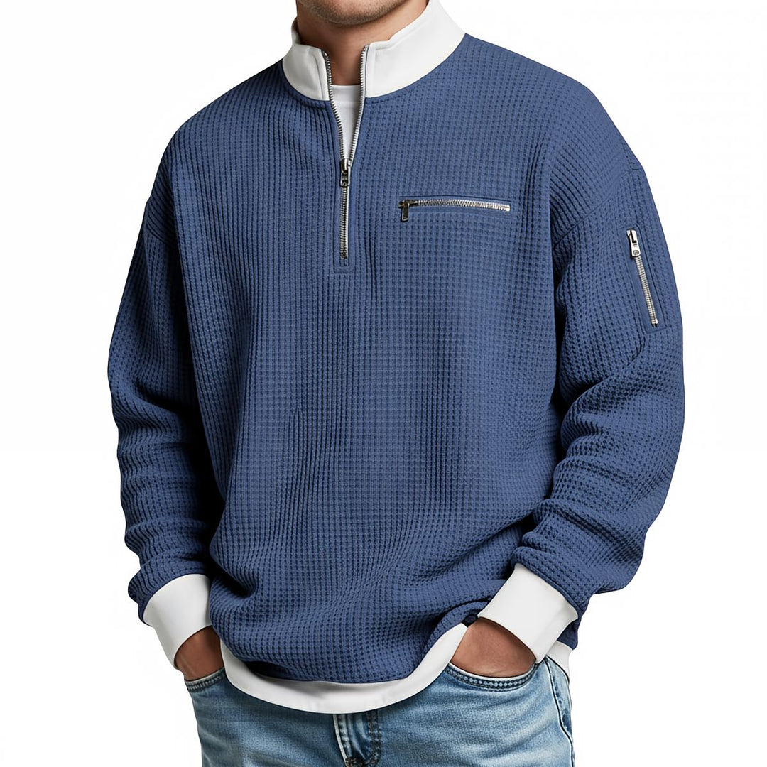 Front view of a blue waffle knit quarter-zip sweater with a white collar, chest zip pocket and zippered sleeve pocket.
