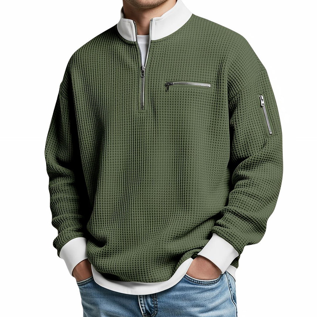 Front view of an olive green waffle knit quarter-zip sweater with a white collar and cuffs, chest zip pocket and sleeve zip pocket.