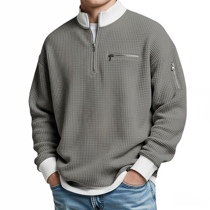 Front view of a gray waffle knit quarter-zip sweater with a white collar and cuffs, chest zip pocket and zippered sleeve pocket.