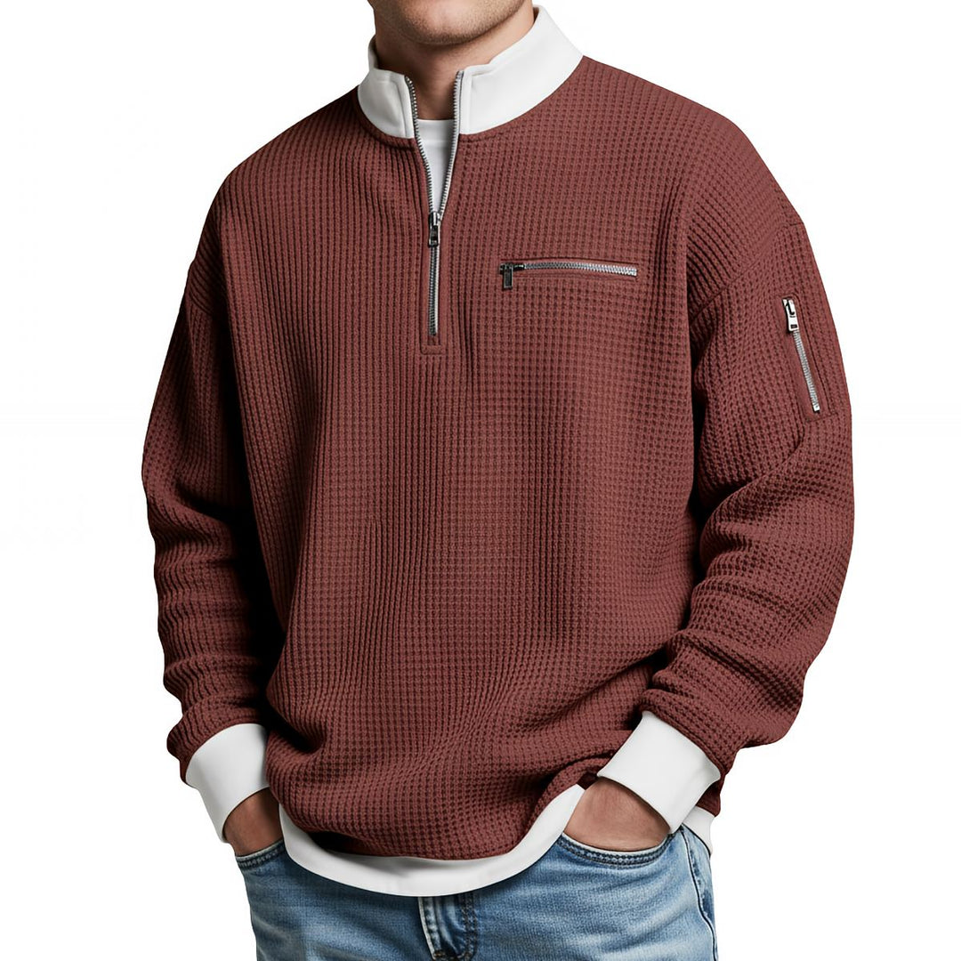Front view of a rust red waffle knit quarter-zip sweater with a white collar and cuffs, chest zip pocket and zippered sleeve pocket.