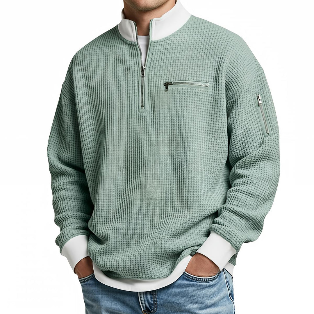 Front view of a sage green waffle knit quarter-zip sweater with a white collar and cuffs, chest zip pocket and sleeve zip.