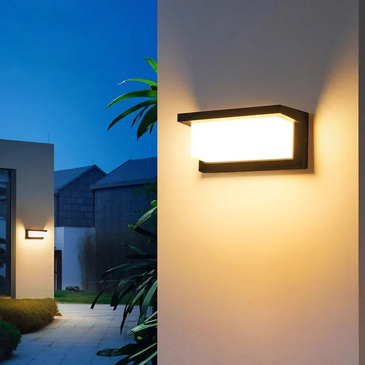 Wall light shining warm glow down a cream exterior wall at twilight, with palm leaves and a garden path nearby. 4